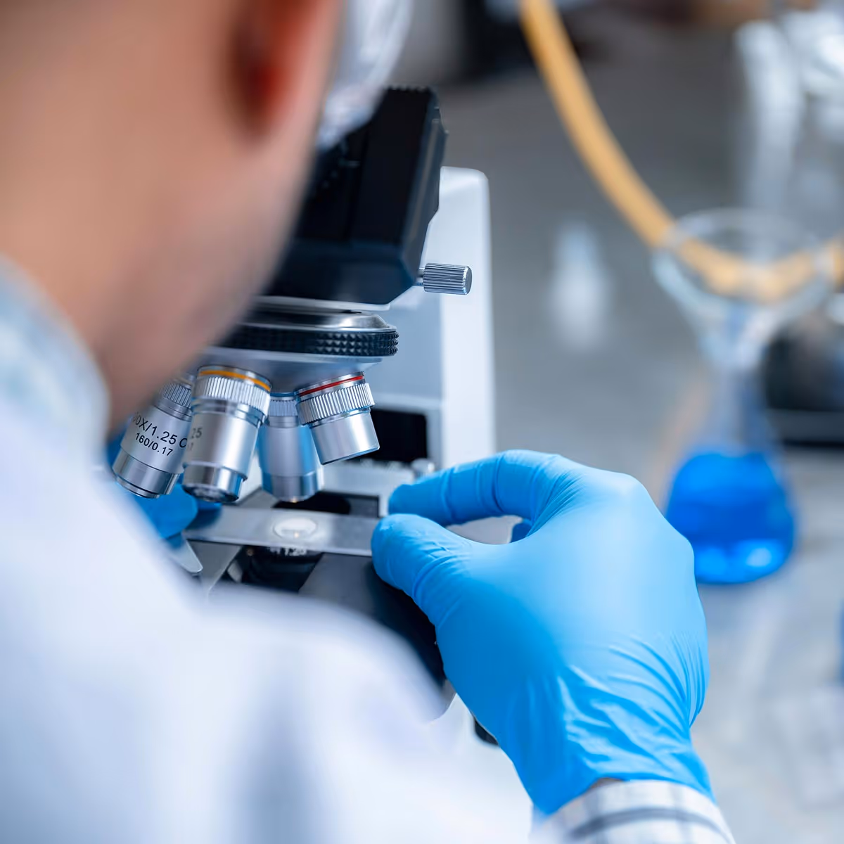 Scientist wearing blue gloves adjusting a microscope slide in a laboratory setting.